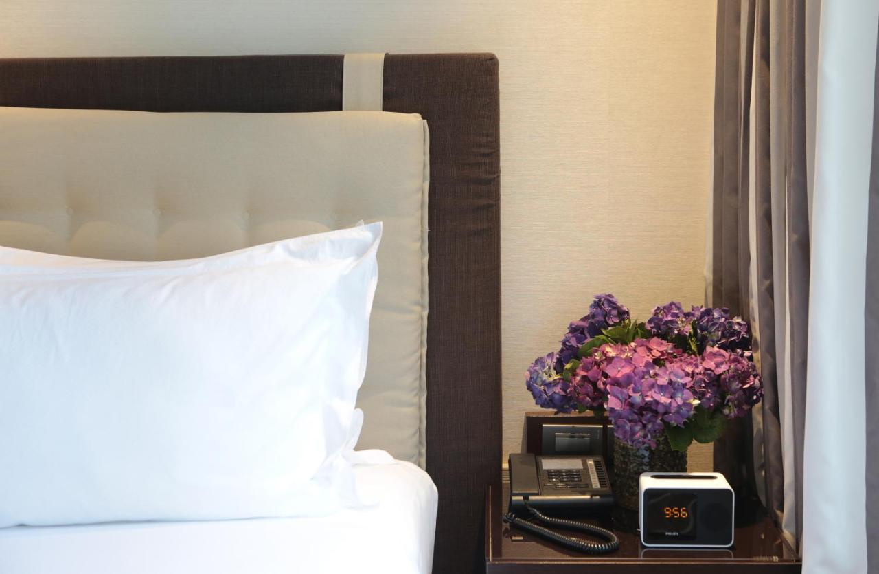 Makati Diamond Residences Макати Экстерьер фото A bedside table with a telephone, a vase of flowers, and a digital alarm clock